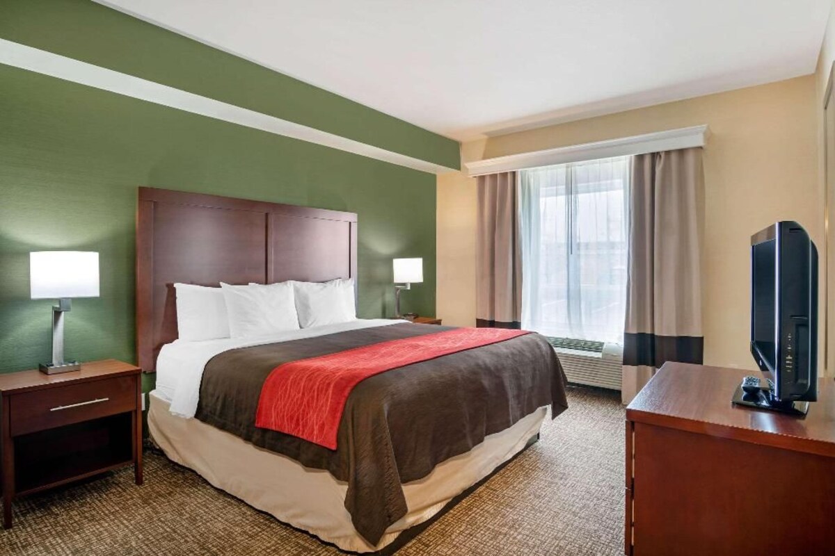 A hotel room with a bed, bedside tables, a TV, and a window with curtains.