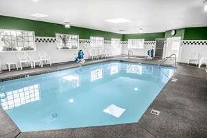 Una piscina con un suelo de baldosas, sillas blancas y un reloj en la pared.