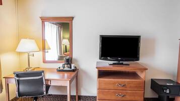 Una camera d'hotel con una scrivania, una sedia, una televisione, uno specchio e un minibar.