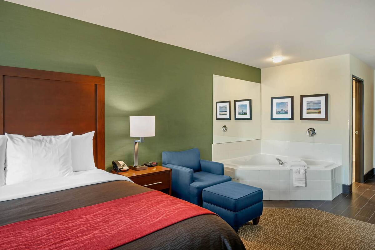 Habitación de hotel con cama, escritorio, silla, bañera grande y espejo.