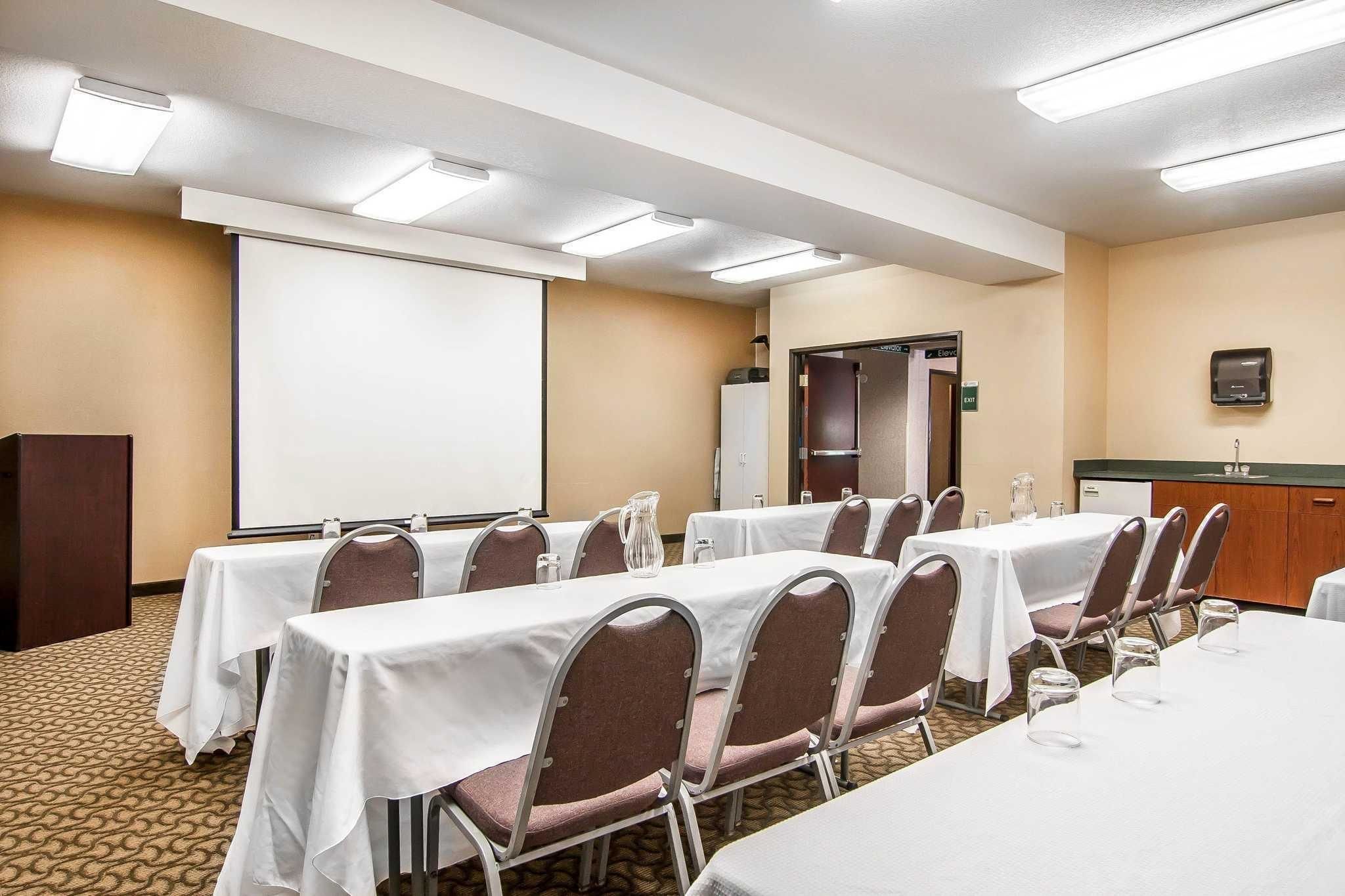 A conference room with tables, chairs, a projector screen, and a whiteboard.