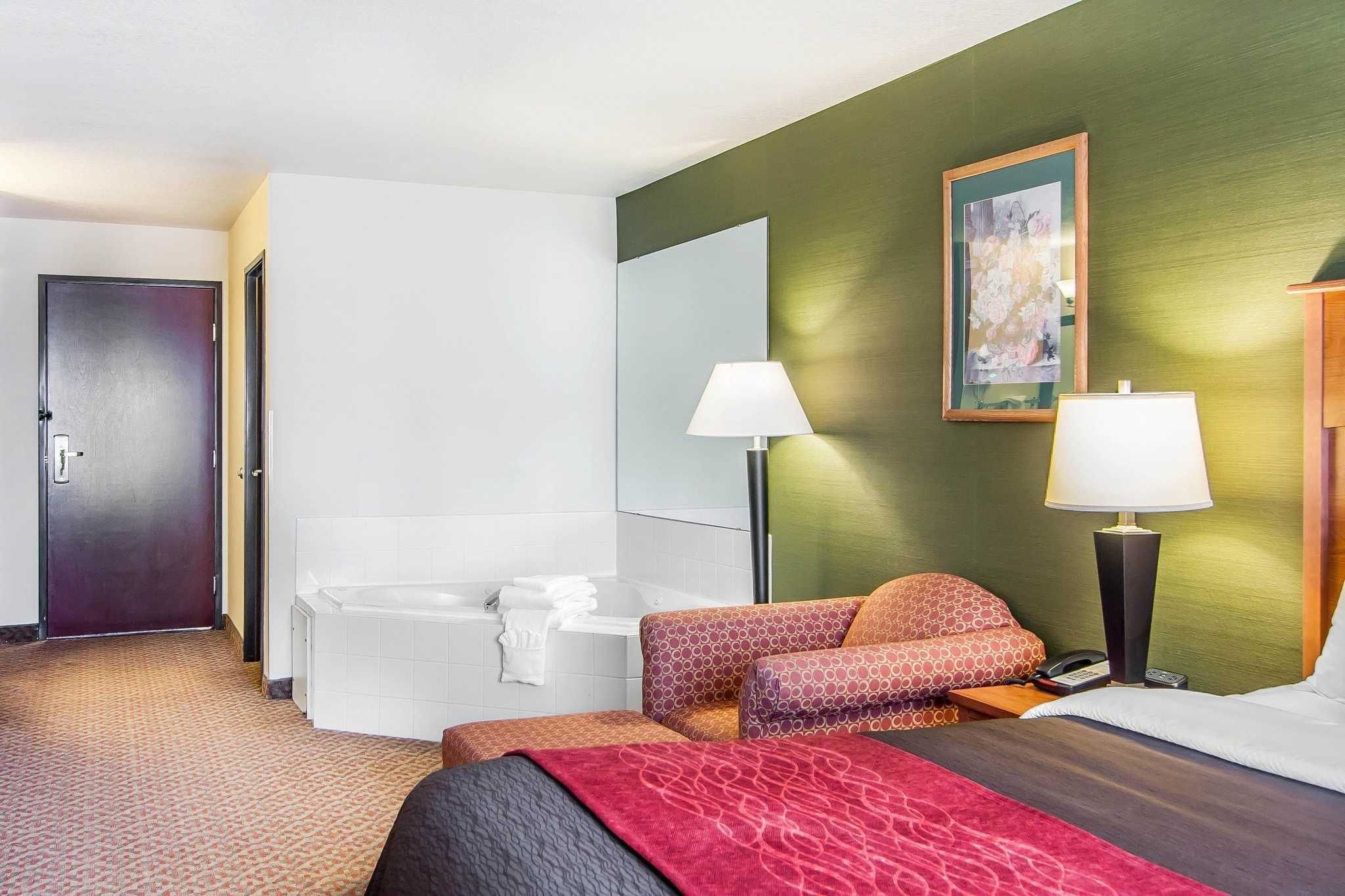 A hotel room with a bed, a sitting area with a sofa, a bathtub, two bedside lamps, and a painting on the wall.