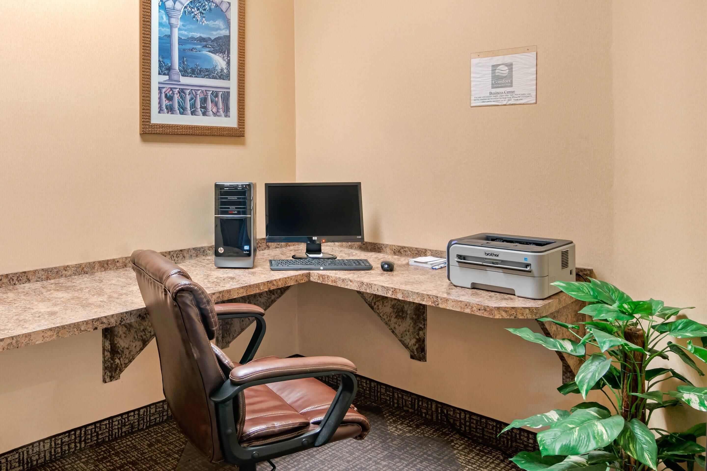 A corner office with a desk, computer, printer, chair, and a framed picture on the wall.