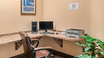 A corner office with a desk, computer, printer, chair, and a framed picture on the wall.