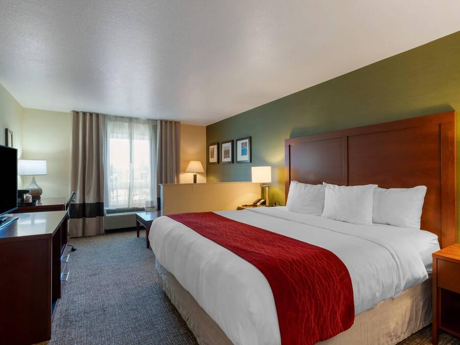 Una habitación de hotel con una cama grande, un escritorio con televisor, una lámpara y una ventana con cortinas.