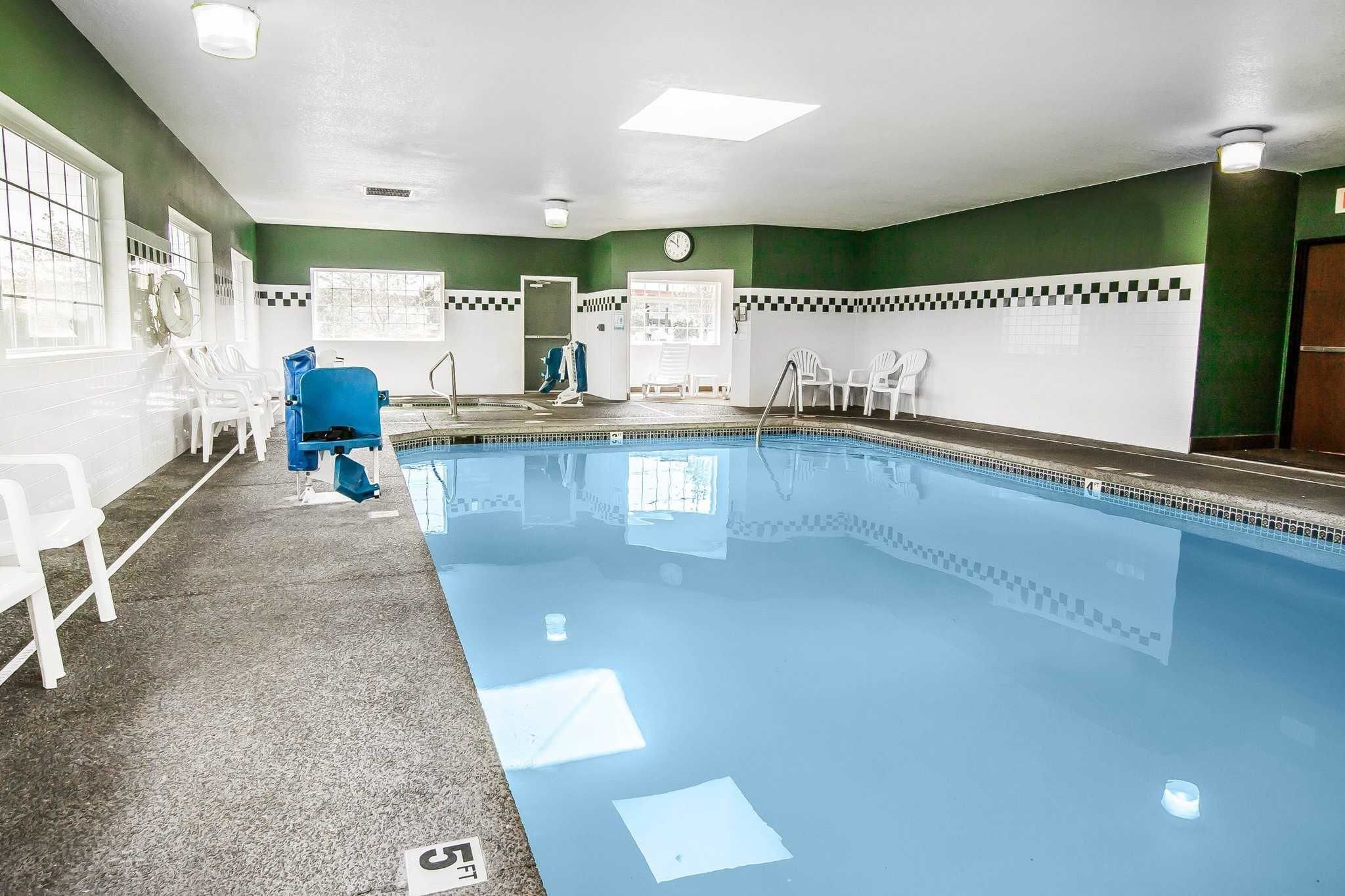 Une piscine intérieure avec un sol carrelé, des chaises blanches et une horloge au mur.