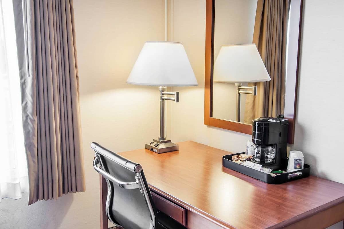 Una habitación de hotel con un escritorio de madera, una lámpara, una cafetera y una silla.