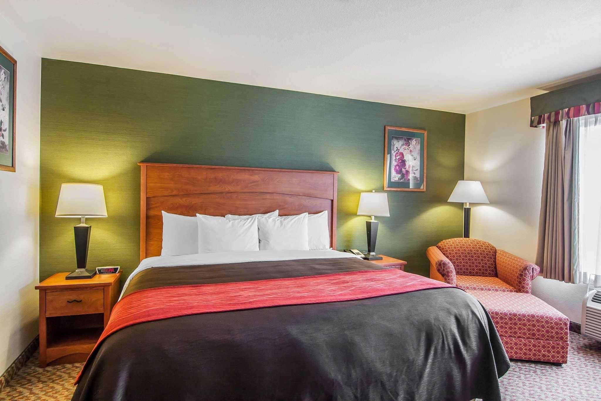 Habitación de hotel con una cama grande, dos mesitas de noche con lámparas, una silla y un cuadro en la pared.