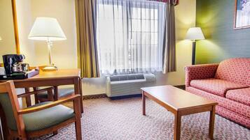 A hotel room with a wooden desk, a red patterned sofa, a patterned carpet, and a window with curtains.