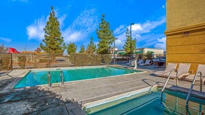 A swimming pool with clear blue water, surrounded by a fence, and equipped with metal ladders. There are lounge chairs and umbrellas in the background.