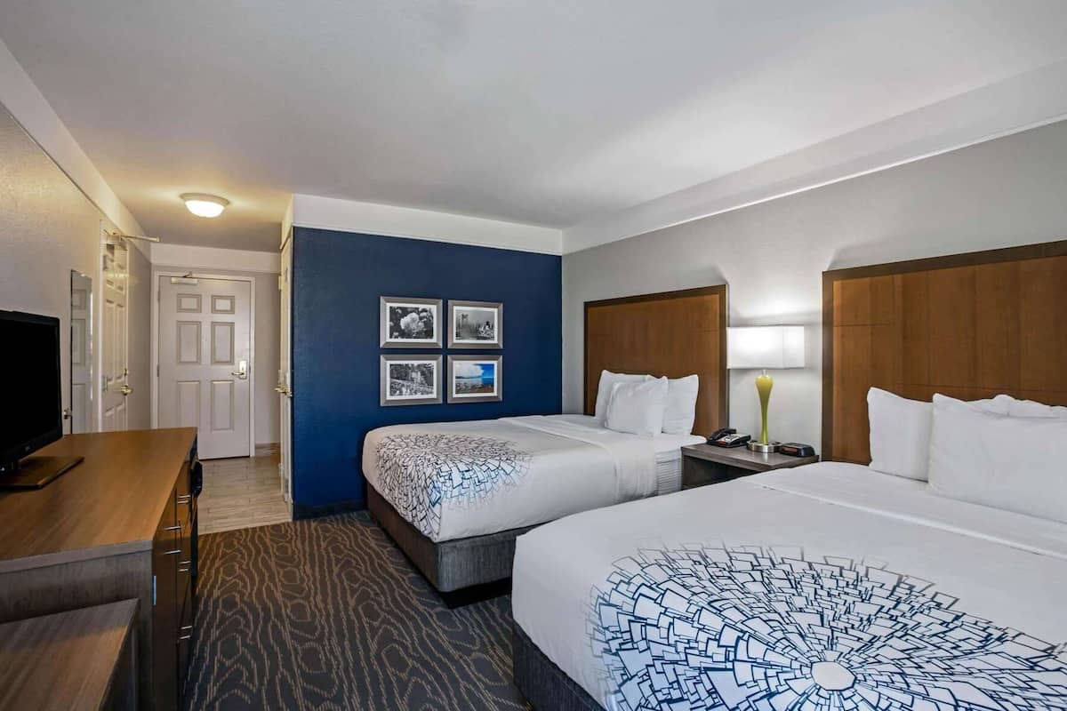 Une chambre d’hôtel avec deux lits, un bureau, une télévision et un mur orné de tableaux.
