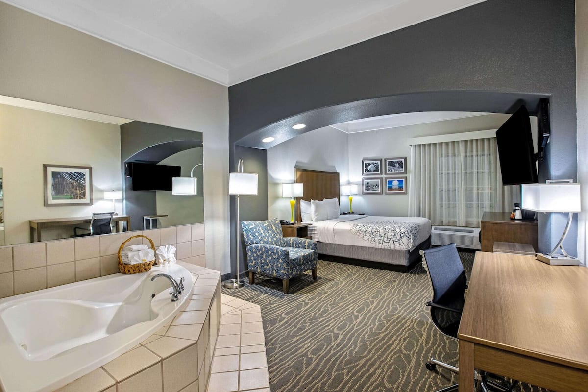 Une chambre d’hôtel avec une grande baignoire, un lit recouvert d’une courtepointe à motifs, un bureau avec une chaise et un téléviseur.