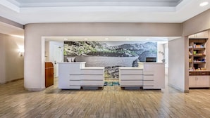 A reception area with a wooden floor, white reception desk, and a large scenic wall mural. - La Quinta Inn & Suites by Wyndham Manteca - Ripon (Ripon)