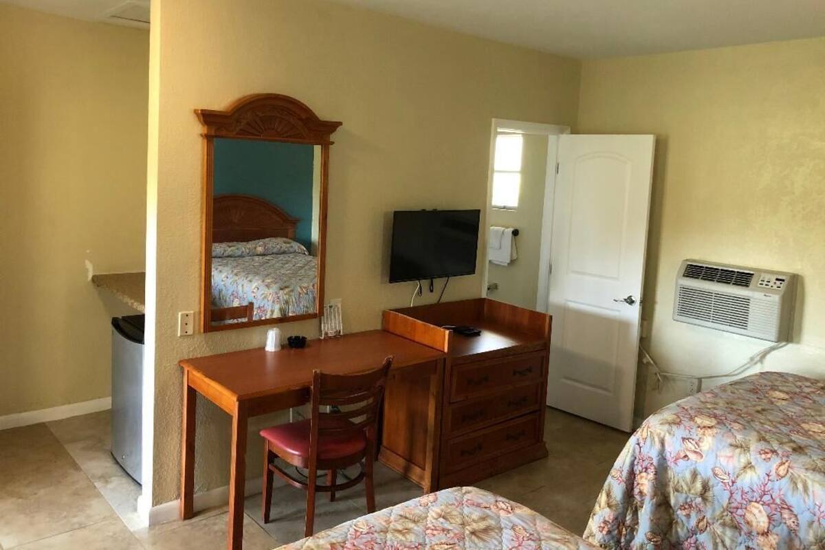 A bedroom with a bed, a desk, a chair, a dresser, a TV, and an air conditioning unit.