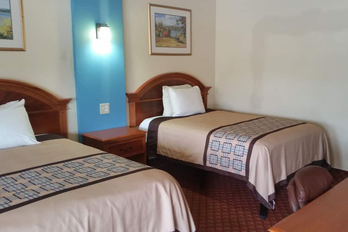 A hotel room with two beds, wooden headboards, a nightstand, a desk, and a framed picture on the wall.