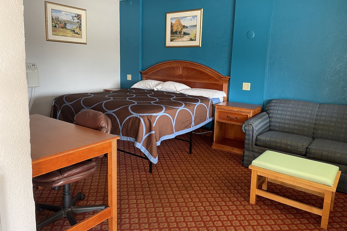 A hotel room with a bed, a desk, a chair, a sofa, and two paintings on the wall.