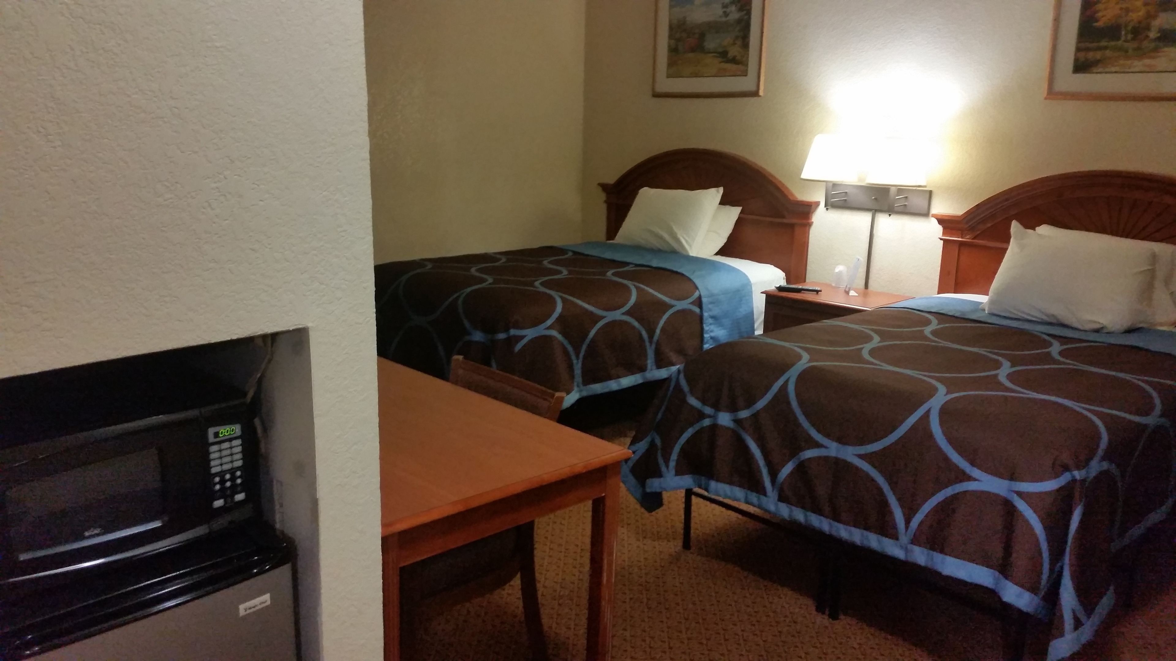 Habitació d'hotel amb dos llits, microones, taula i taulell de nit amb làmpada.