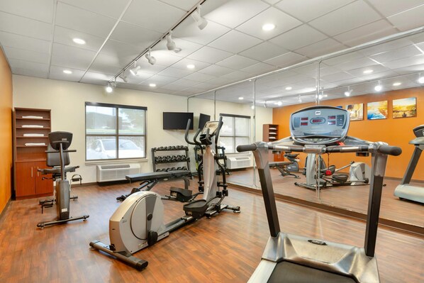 A gym with various exercise equipment, a large mirror, and a television on the wall.
