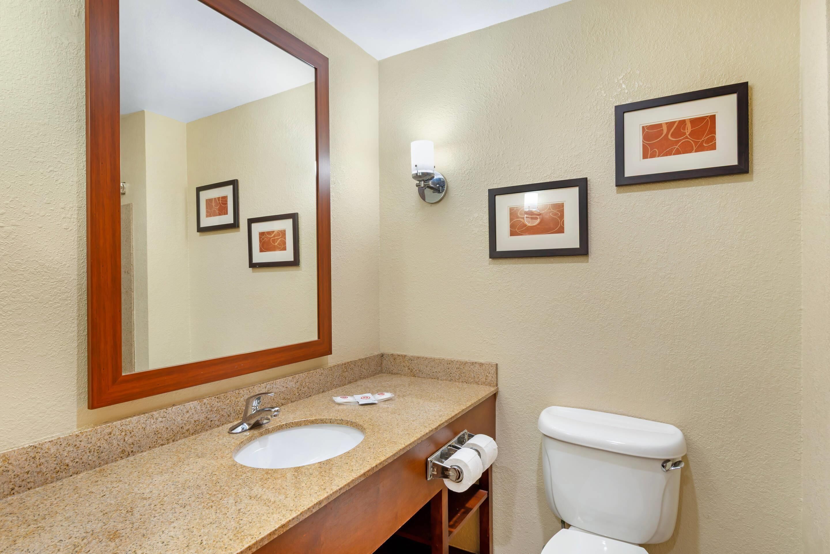 Une salle de bain avec un lavabo, un miroir, des toilettes et des tableaux encadrés accrochés au mur.