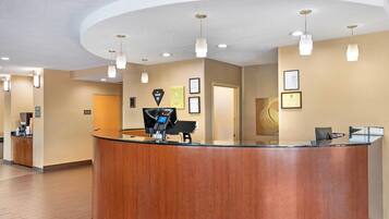 A reception desk with a wooden finish, a digital kiosk, and a framed certificate on the wall.
