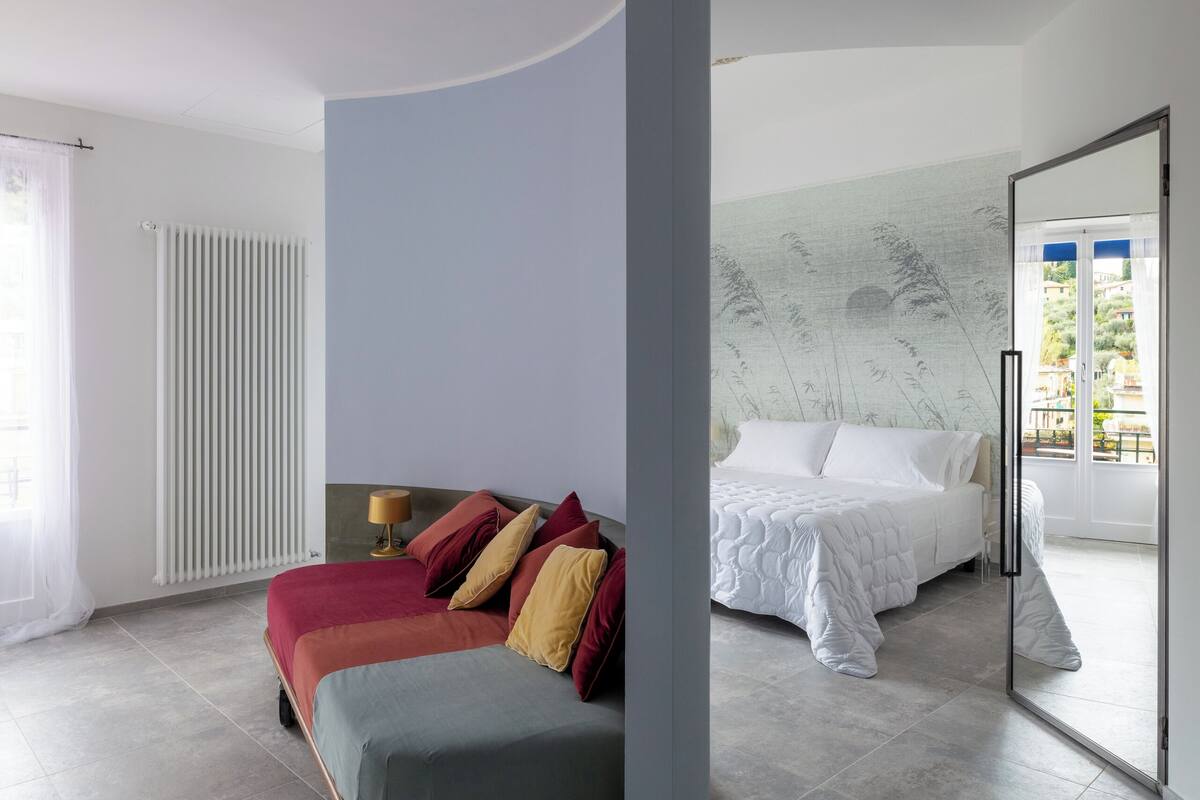 A modern bedroom with a bed, a sofa, and a large window.