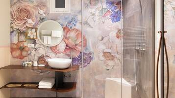 A bathroom with a large floral mural, a round mirror, a sink, and a glass-enclosed shower.