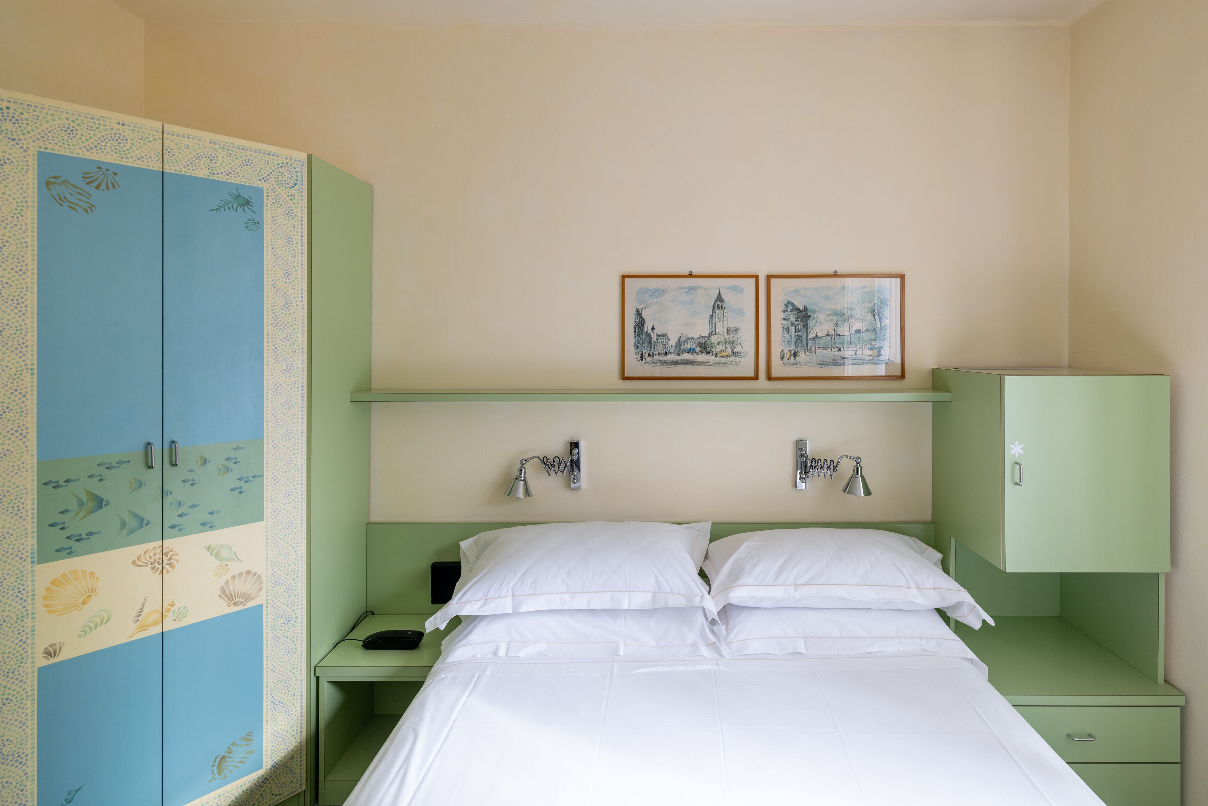 Une chambre à coucher comprenant un lit, deux tables de chevet, une commode, une armoire et deux tableaux encadrés accrochés au mur.