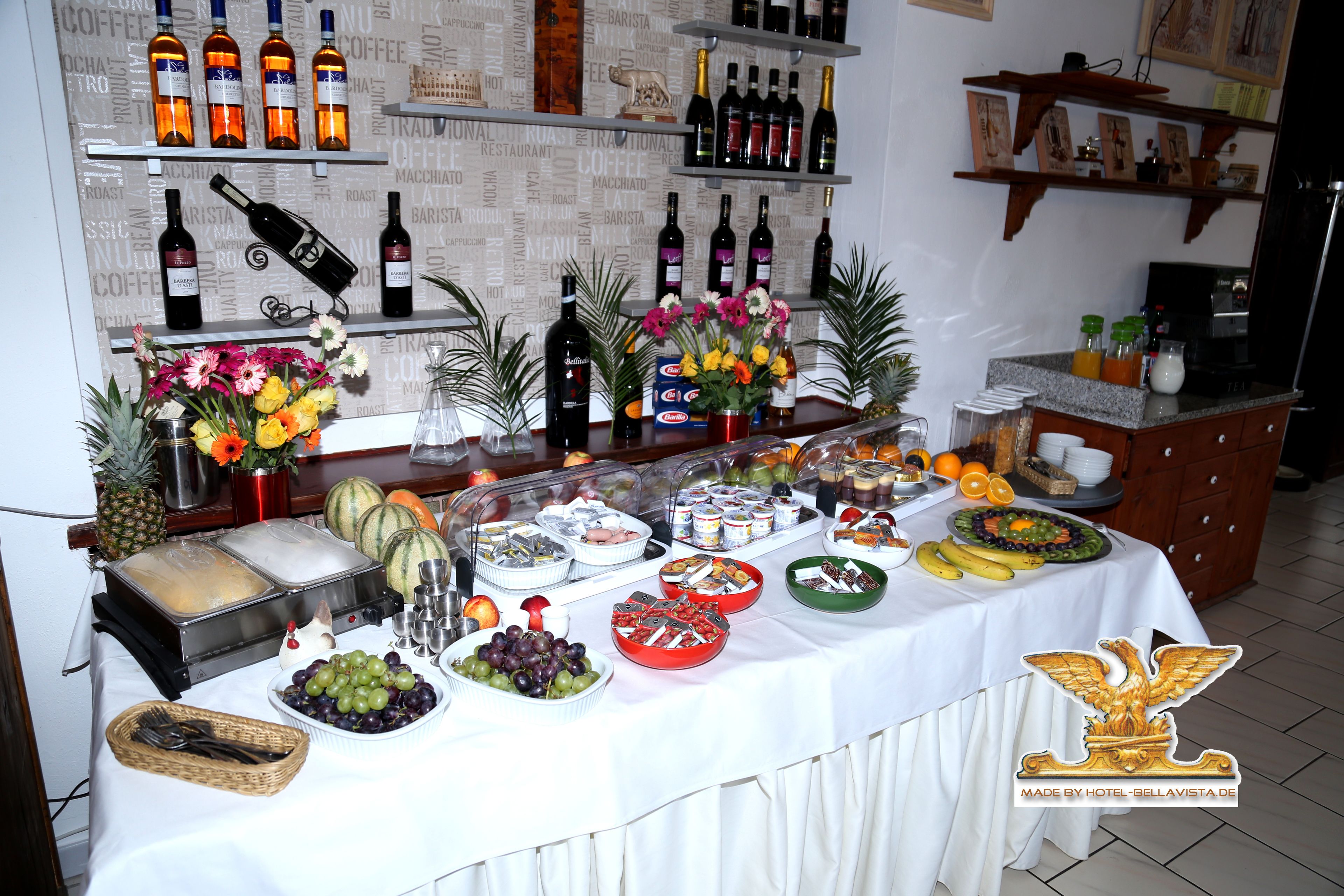 A buffet setup with various food items, a wine selection, and decorative flowers.
