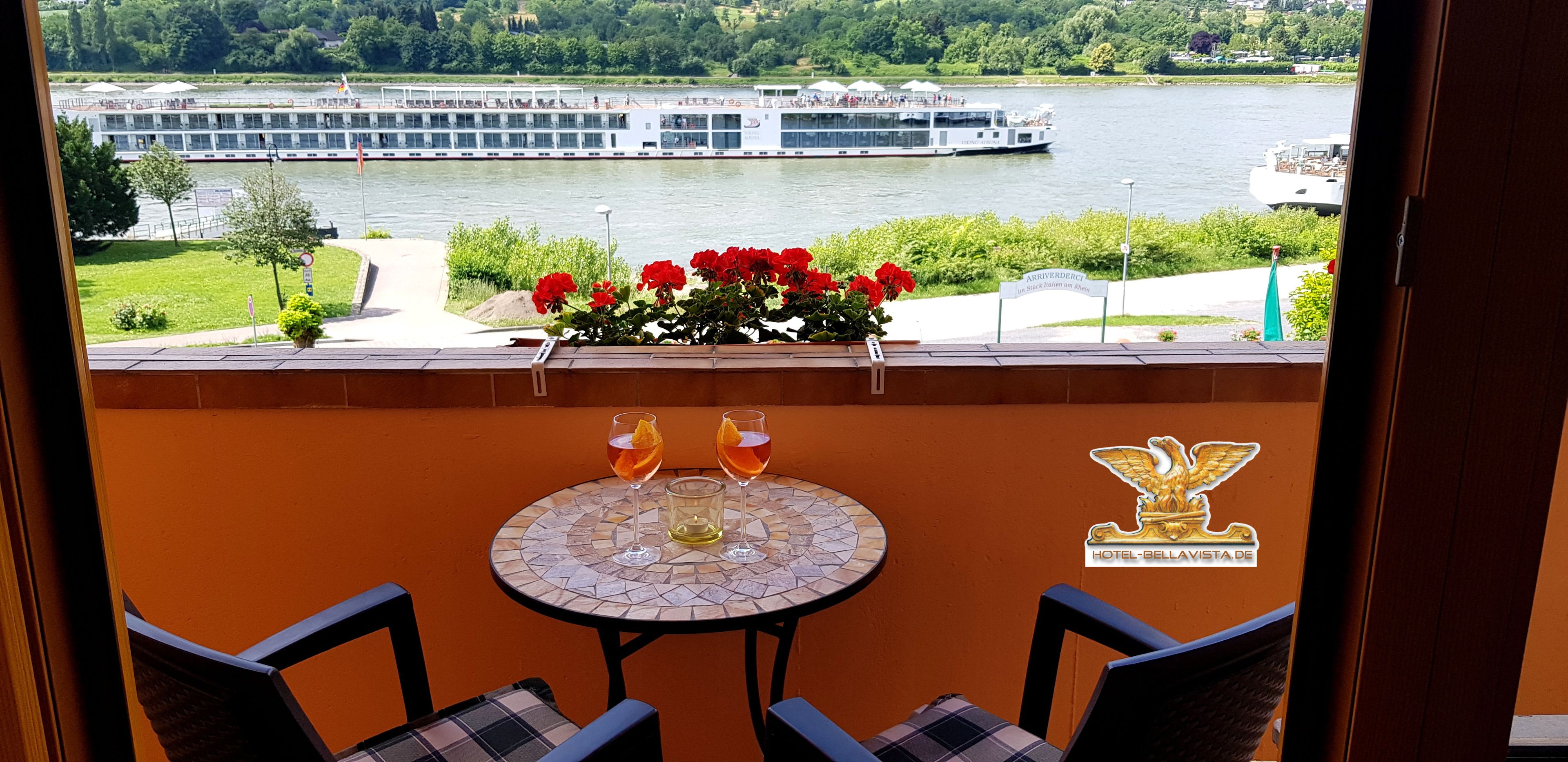 Ein Balkon mit Tisch und Stühlen, einer Blumenkomposition und Blick auf einen Fluss mit Booten.