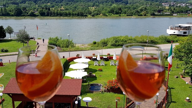 Two glasses of wine with a view of a lake and outdoor seating area.