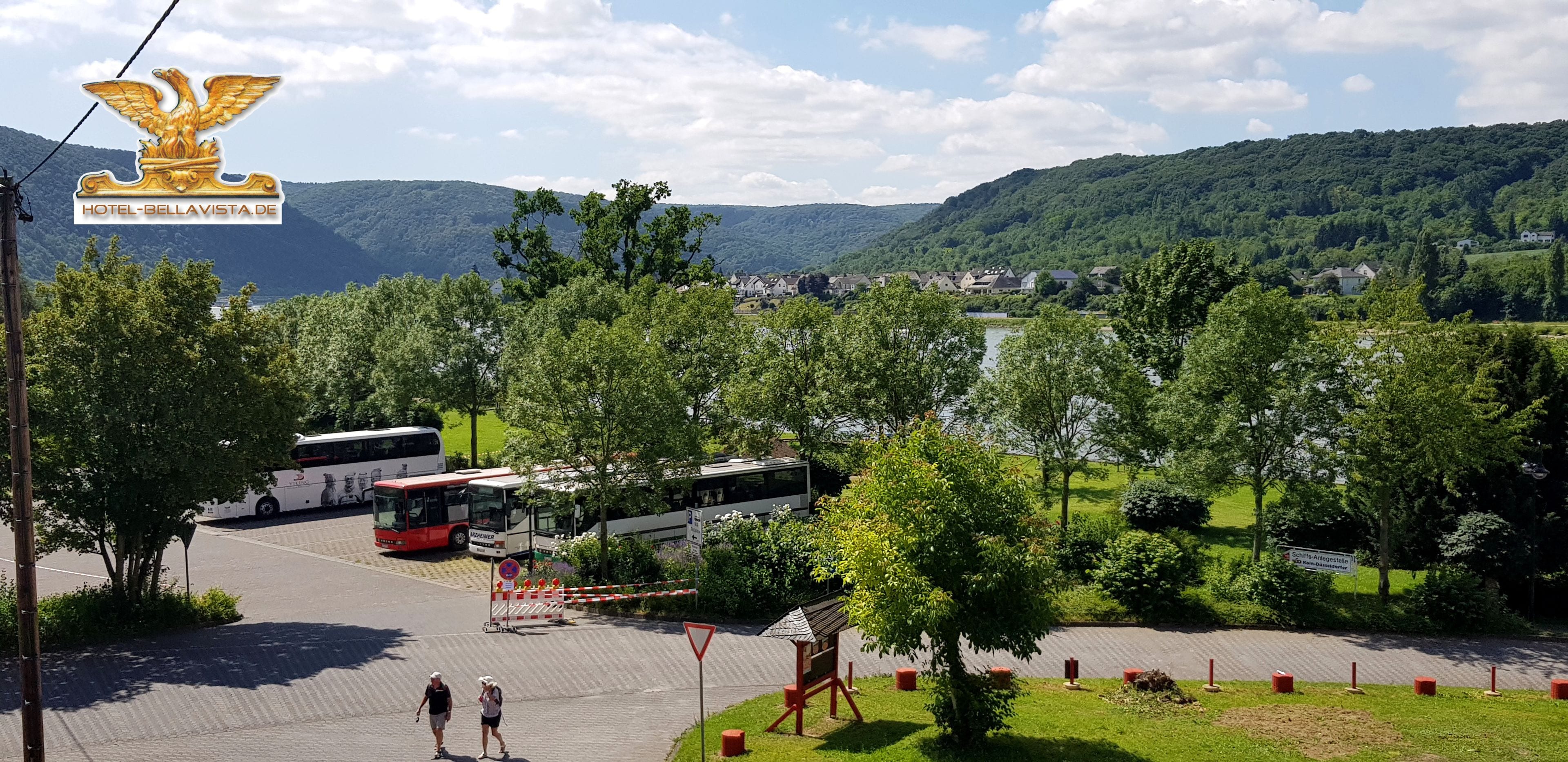 A bus station with multiple buses, a playground, and a scenic view of a town and mountains in the background.