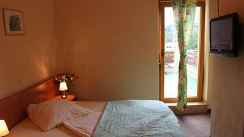 Una habitación de hotel con cama, televisor, mesita de noche con lámpara y ventana con cortina.