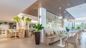 Egy modern szállodai előtér, pihenőhelyekkel, recepcióval és egy nagy növénygyel.