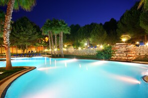 A nighttime swimming pool with lounge chairs and palm trees.