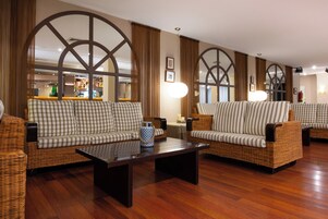 Un vestíbulo con sofás de mimbre, una mesa de centro y grandes ventanas con cortinas.