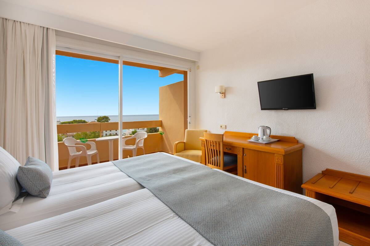 Ein Hotelzimmer mit einem großen Bett, einem Schreibtisch mit Stuhl, einem Fernseher und einem Balkon mit Blick.