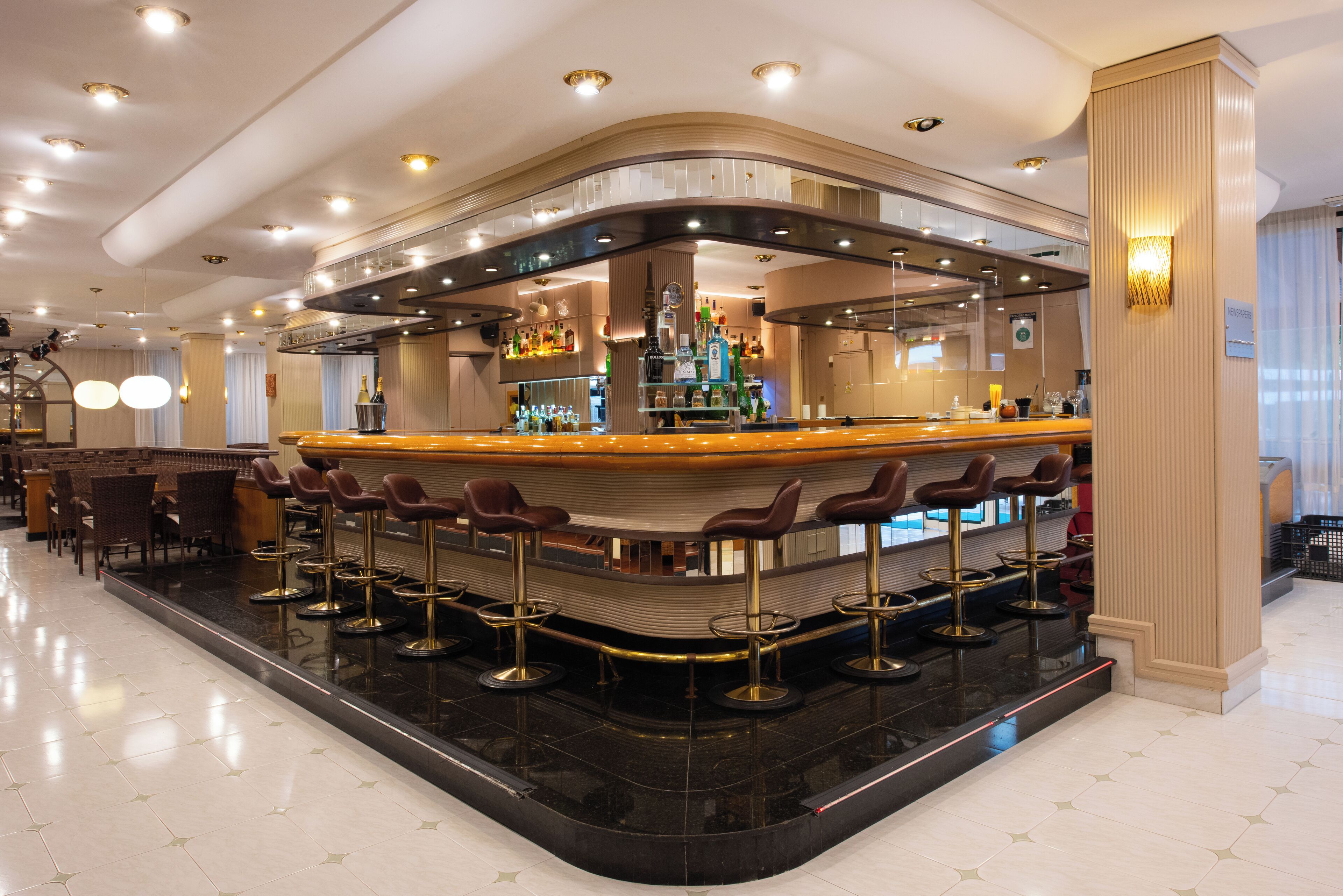 Una zona de bar con una barra curva, varios taburetes y un techo bien iluminado.