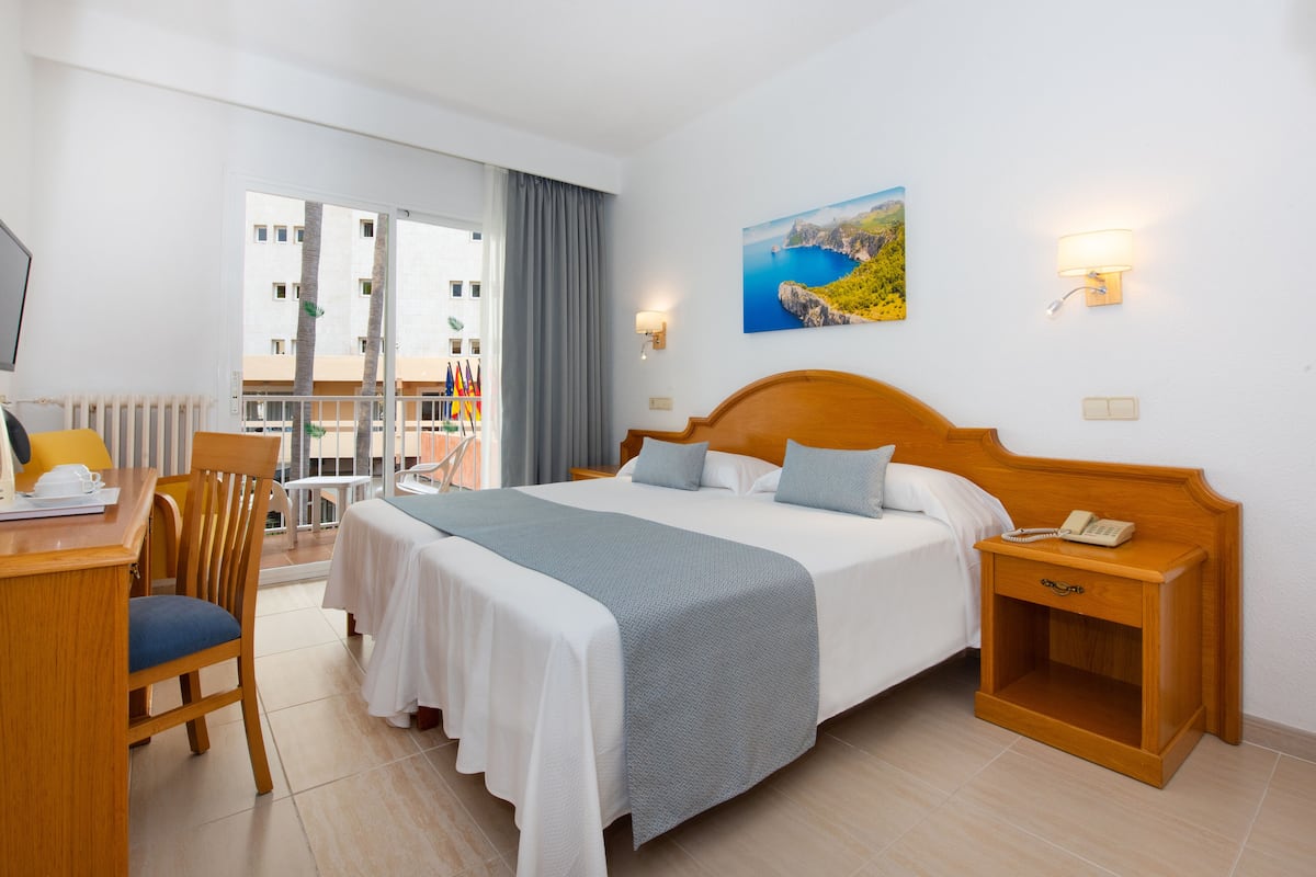 Ein Hotelzimmer mit Bett, Nachttisch, Stuhl, Schreibtisch und Blick auf den Balkon.