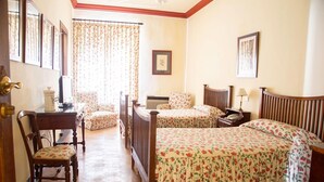 A room with two beds, a chair, a desk, and a window with floral curtains. - Cortijo el Esparragal (Gerena)
