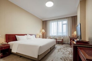 A hotel room with a large bed, bedside tables, a TV, and a seating area with a chair and table. - Liaoning Zhengxie Hotel (Shenyang)