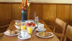 Une table de petit-déjeuner dressée avec des croissants, du jus d’orange, du café et un vase rempli de fleurs.