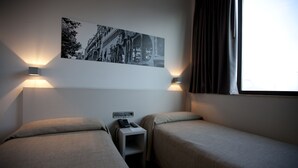 Une chambre d’hôtel avec deux lits simples, une table de chevet avec un téléphone et un tableau accroché au mur.