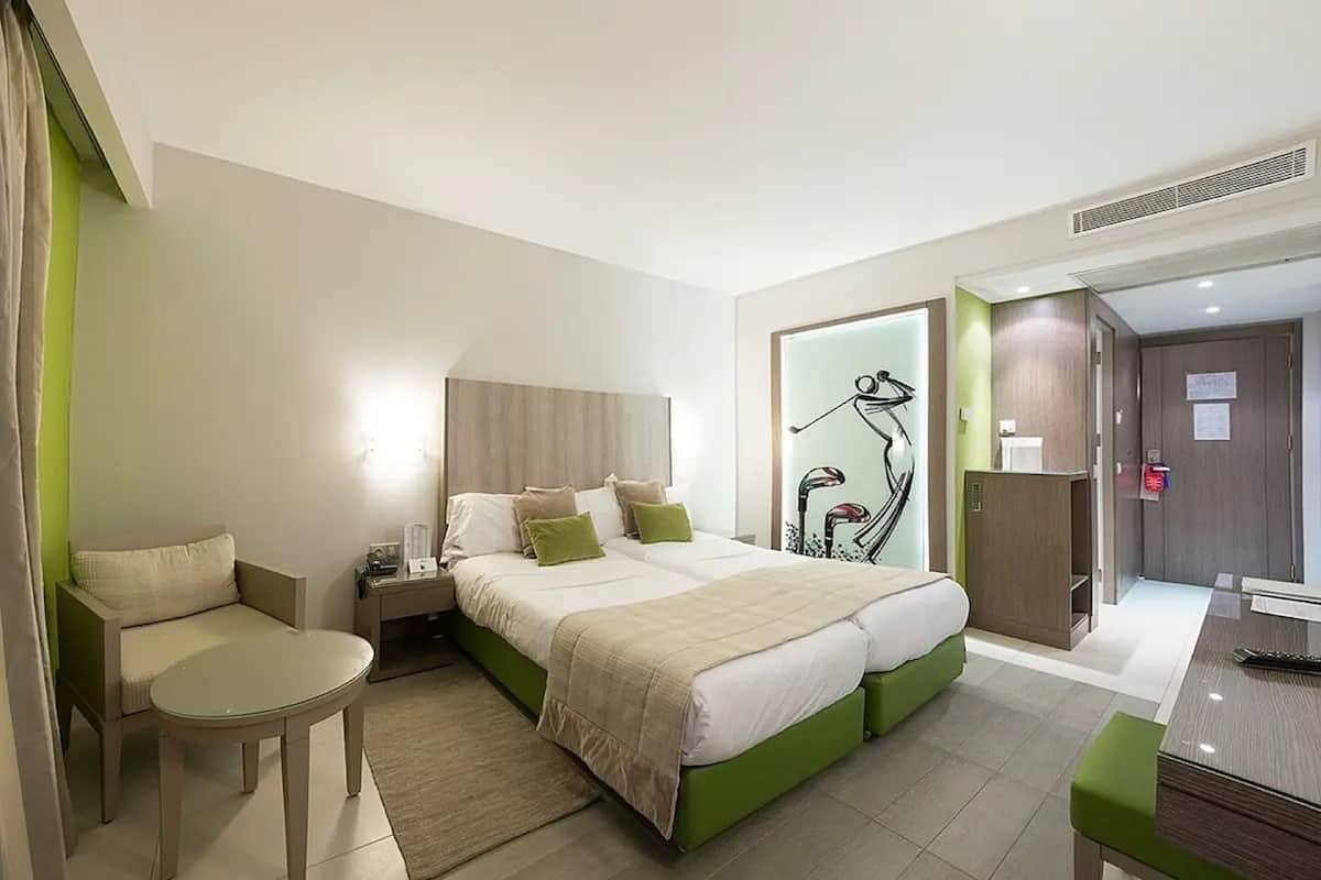 Ein Hotelzimmer mit Bett, Nachttisch, Sessel und Schreibtisch mit Stuhl.
