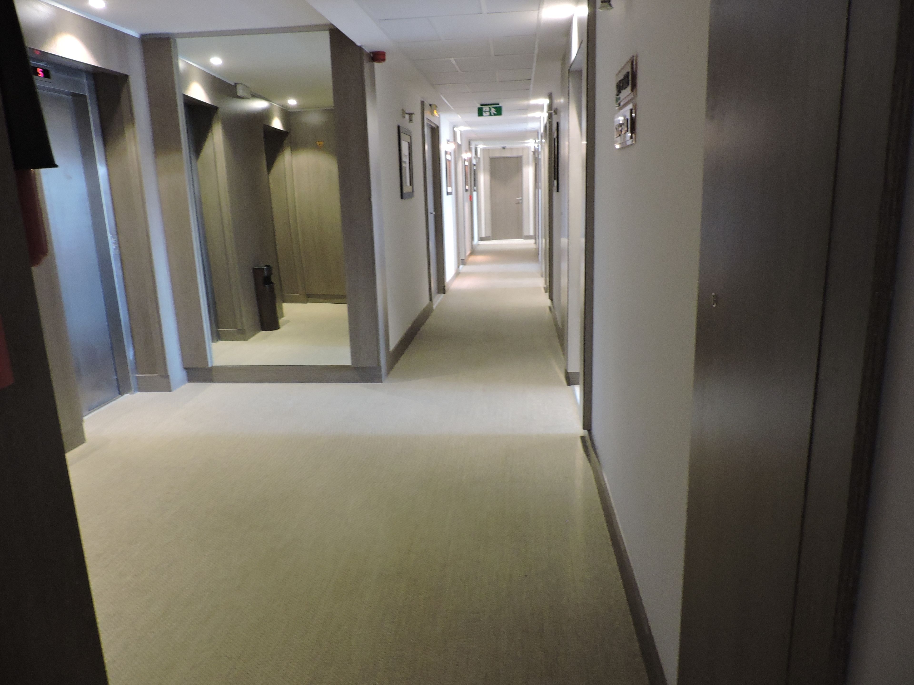 Pasillo de hotel con varias puertas, suelo alfombrado e iluminación empotrada en el techo.