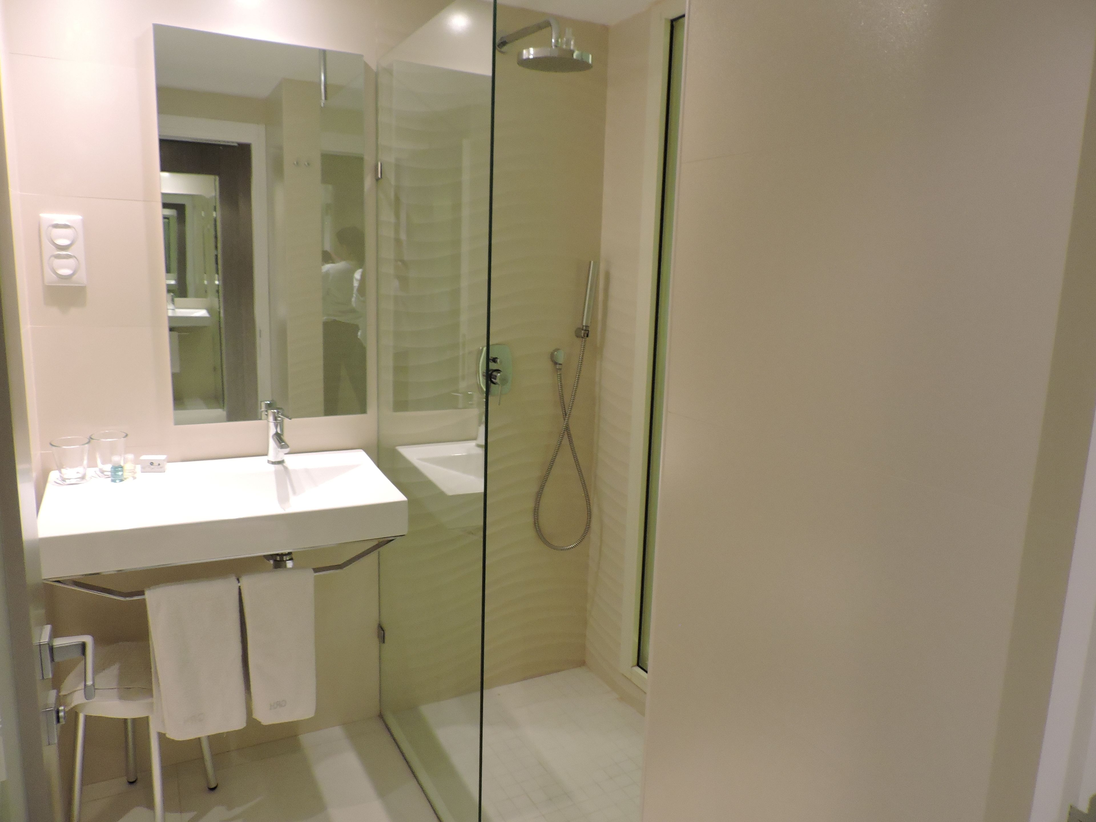 A modern bathroom with a glass-enclosed shower, a white sink, and a mirror above it.
