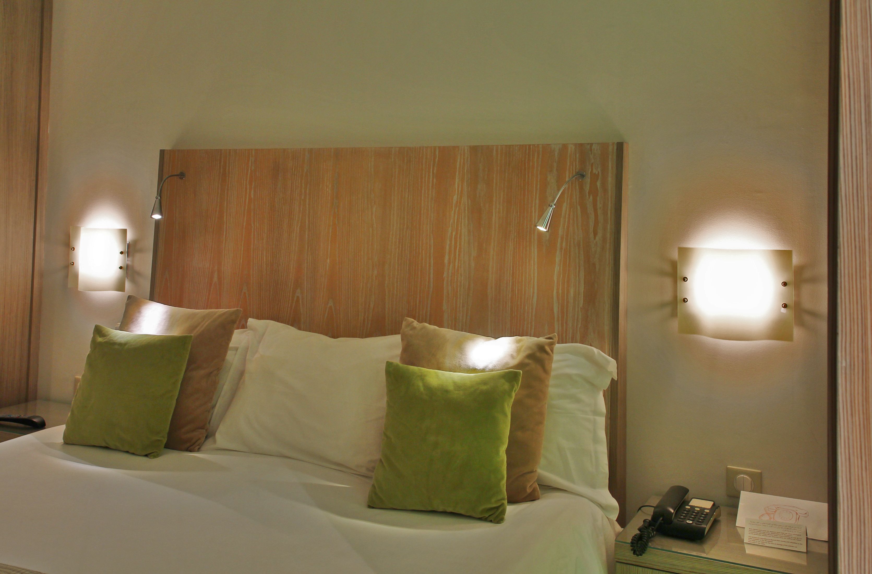 A hotel room with a wooden headboard, two bedside lamps, a telephone, and a notepad on the nightstand.