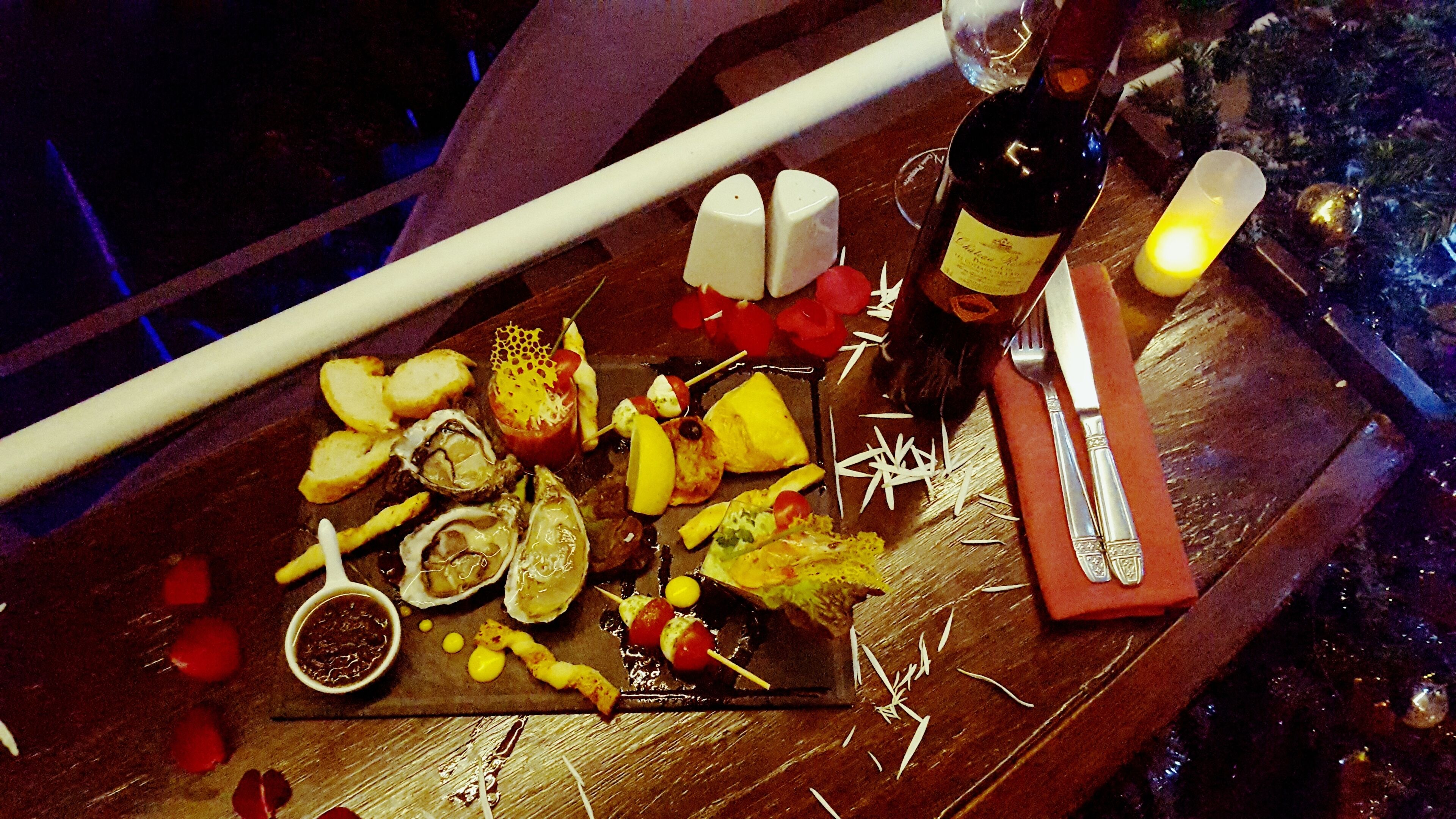 A wooden table with a variety of food items, including oysters, bread, and a bottle of wine.