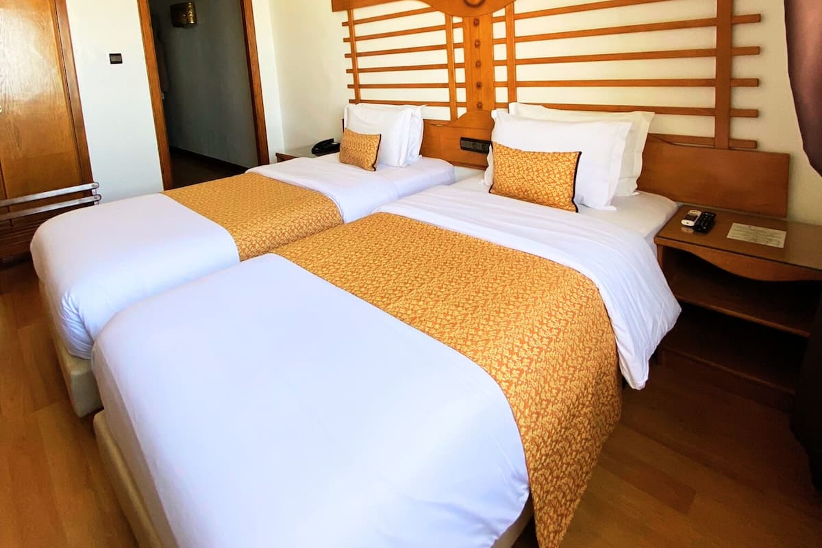 Une chambre d’hôtel avec deux lits, une tête de lit en bois et une table de chevet avec une télécommande.