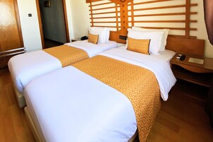 Ein Hotelzimmer mit zwei Betten, einem Holzkopfteil und einem Nachttisch mit Fernbedienung.