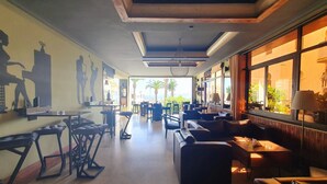 A spacious lounge area with a long table, several chairs, and a sofa. There are large windows providing a view of the outdoors. - Hotel Rembrandt (Tangier)